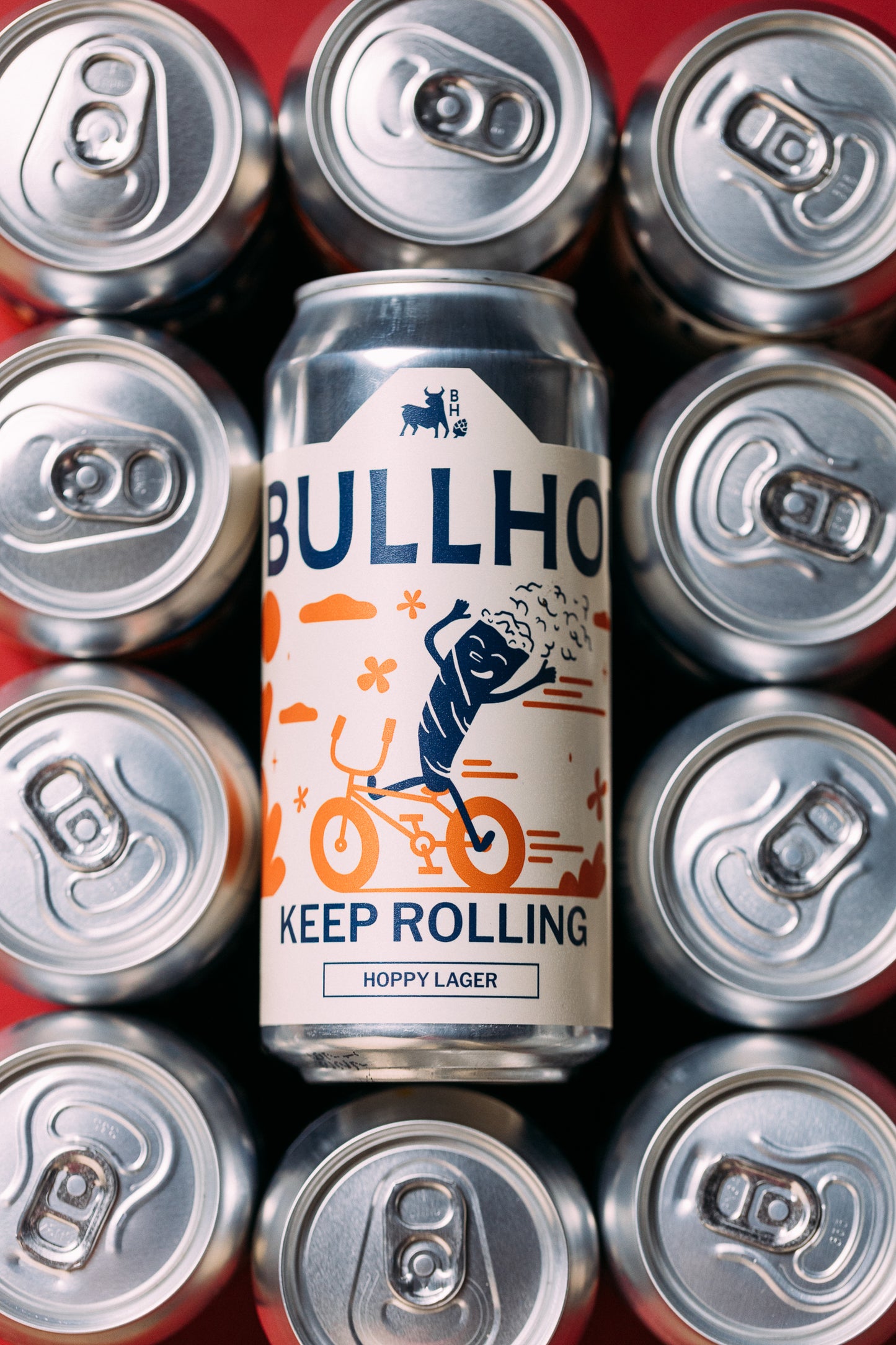 
                  
                    Bullhouse Brewery Keep Rolling beer can surrounded by silver beer cans on a red background
                  
                