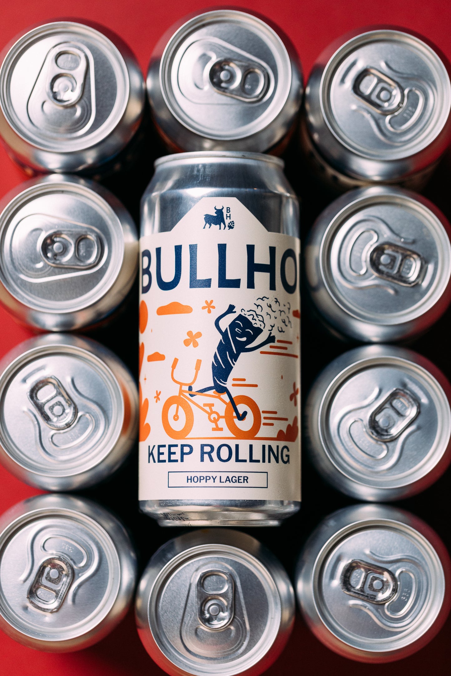 
                  
                    Bullhouse Brewery Keep Rolling beer can surrounded by silver cans on a red background
                  
                